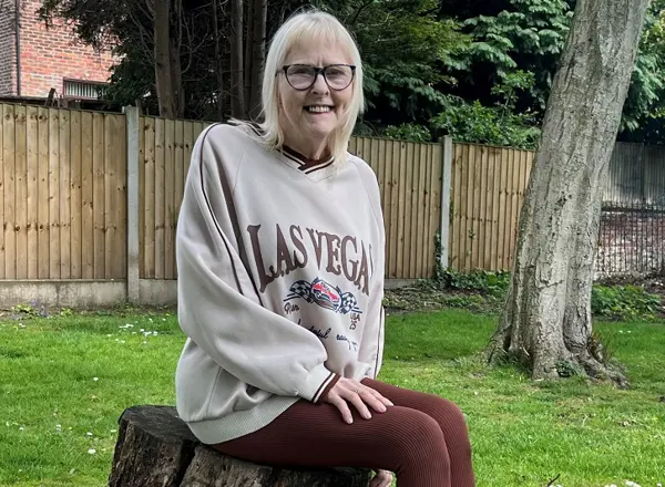 A photo of Christie patient Jan Smith sitting on a tree stump.