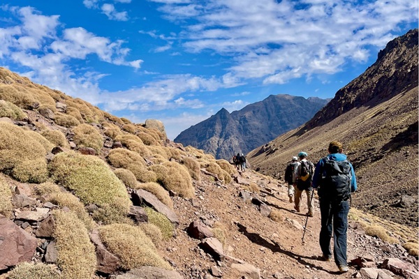 A photo of a trek in Morocco with hikers in the foreground and mountains in the background.