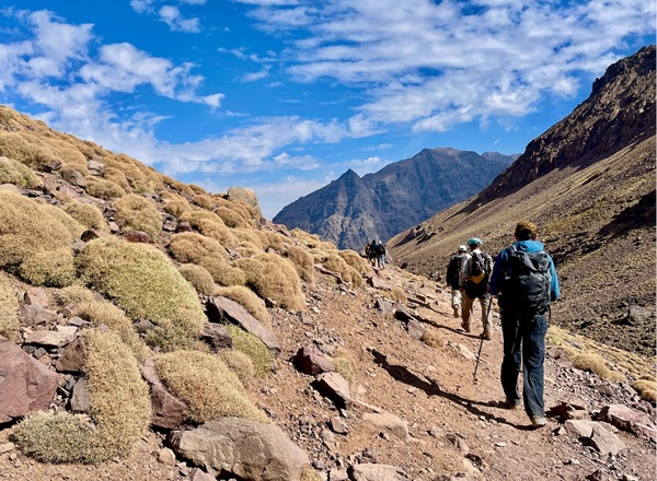 A photo of a trek in Morocco with hikers in the foreground and mountains in the background.
